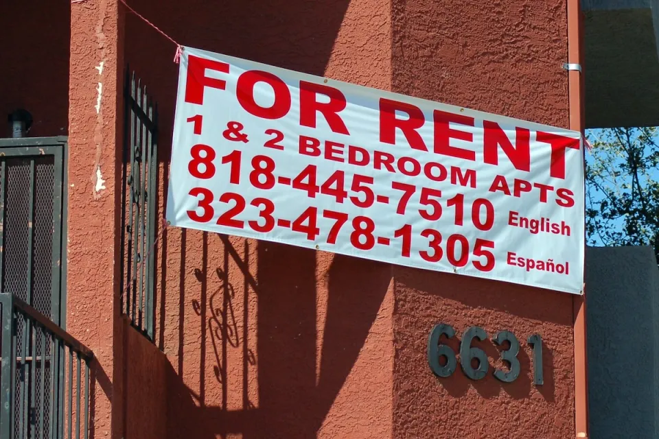 For Rent sign on red stucco apartment building.